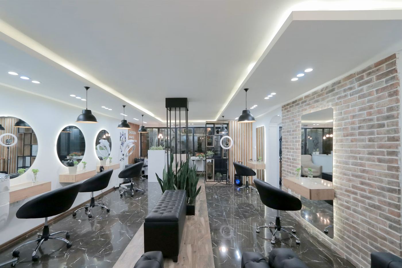 Finished salon build-out by Harrison Building Co — styling stations with lit mirrors, oak floating counters, an exposed brick accent wall and a polished marble floor