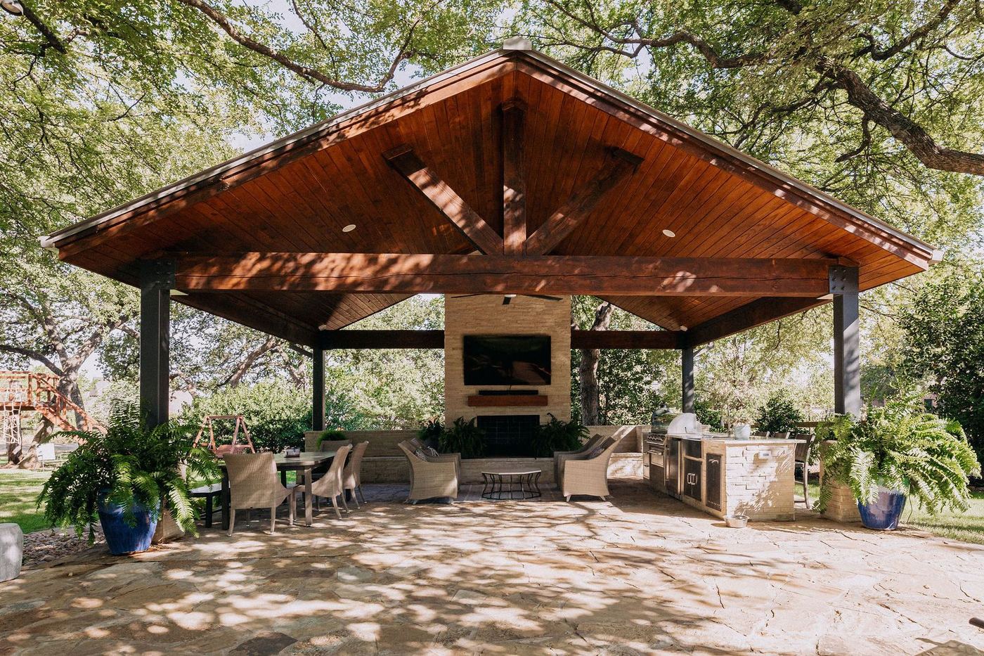 Stone pavilion with stained timber trusses beside a custom pool in North Texas