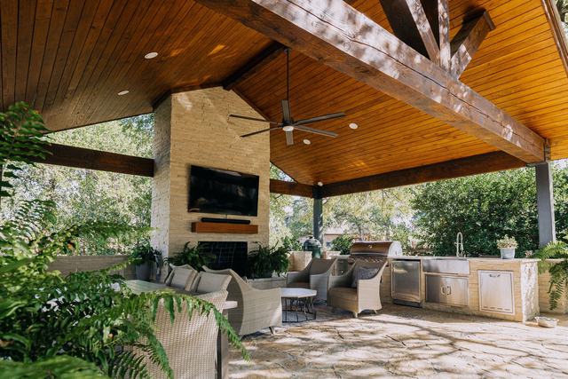 Covered outdoor pavilion with a stained tongue-and-groove ceiling, stone fireplace, and built-in outdoor kitchen