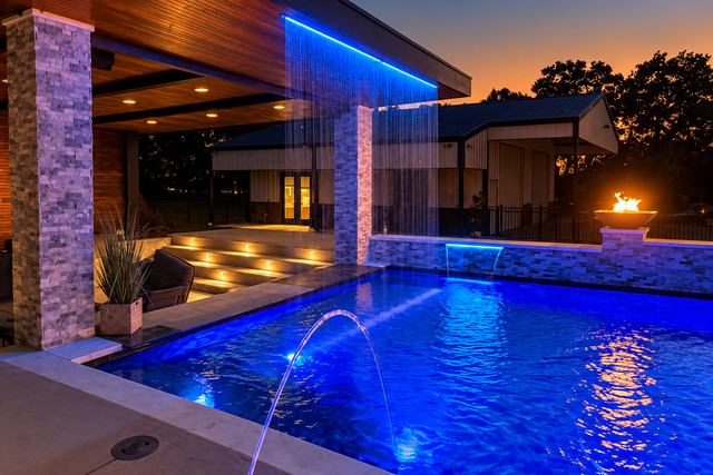 Custom gunite pool at twilight with deck jets, LED lighting, a fire bowl, and a covered patio in Tarrant County