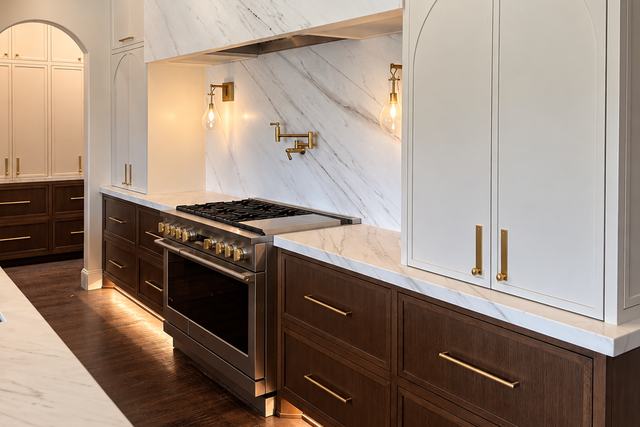 Kitchen range wall with a full-height marble slab surround, brass pot filler, and walnut base cabinets