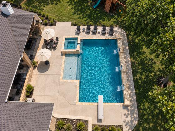 Aerial view of a custom pool and raised spa with travertine decking, shade umbrellas and a lounge area