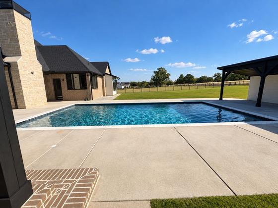 Custom pool beside a covered pavilion with a stone chimney