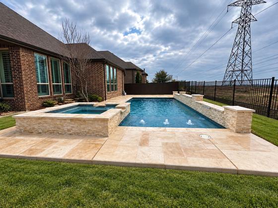 Gunite pool with a raised spa and spillways over travertine decking