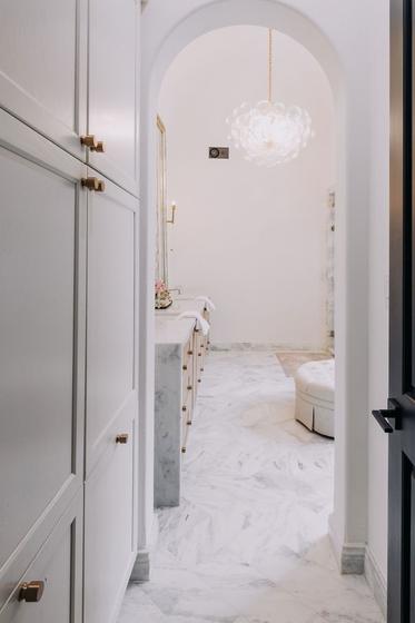 Arched opening into a marble primary bathroom with a hanging light fixture