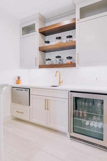 Beverage bar with walnut floating shelves, a glass-front wine fridge and marble backsplash