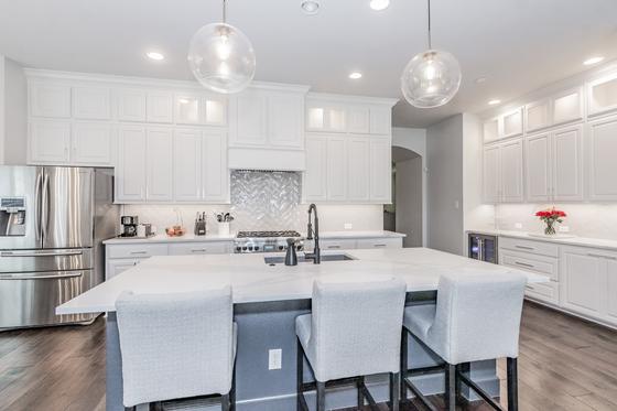 Open white kitchen remodel with a waterfall quartz island, glass globe pendants and upholstered bar seating