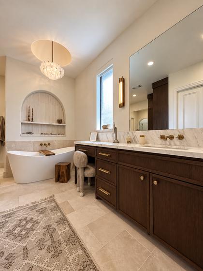 Primary bathroom remodel with a freestanding tub in an arched alcove, walnut vanity and travertine floor
