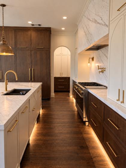Kitchen remodel with walnut cabinetry, a full-height marble range wall, brass pulls and under-cabinet lighting