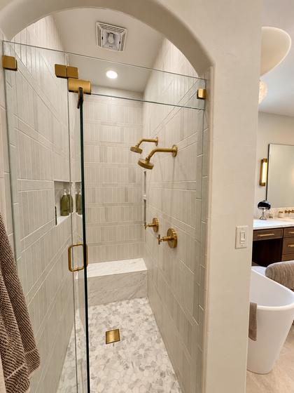 Walk-in shower with a marble-look tile surround, arched opening and brass fixtures