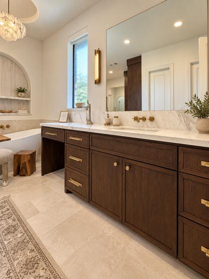 Double vanity in a primary bathroom remodel with walnut cabinetry, a marble counter and brass sconces