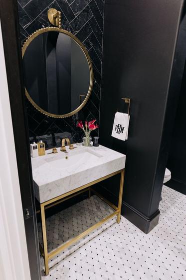 Powder room remodel with a black herringbone tile wall and a marble console sink