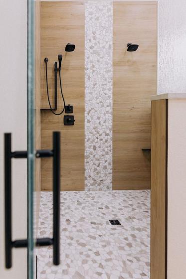 Curbless walk-in shower with wood-look tile, a pebble floor and matte black fixtures