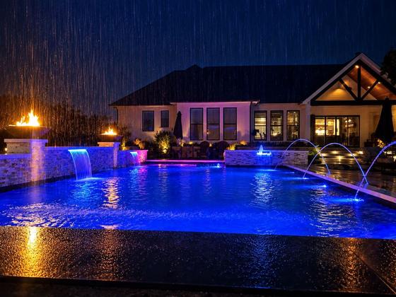 Custom pool at night with lit waterfalls and fire bowls